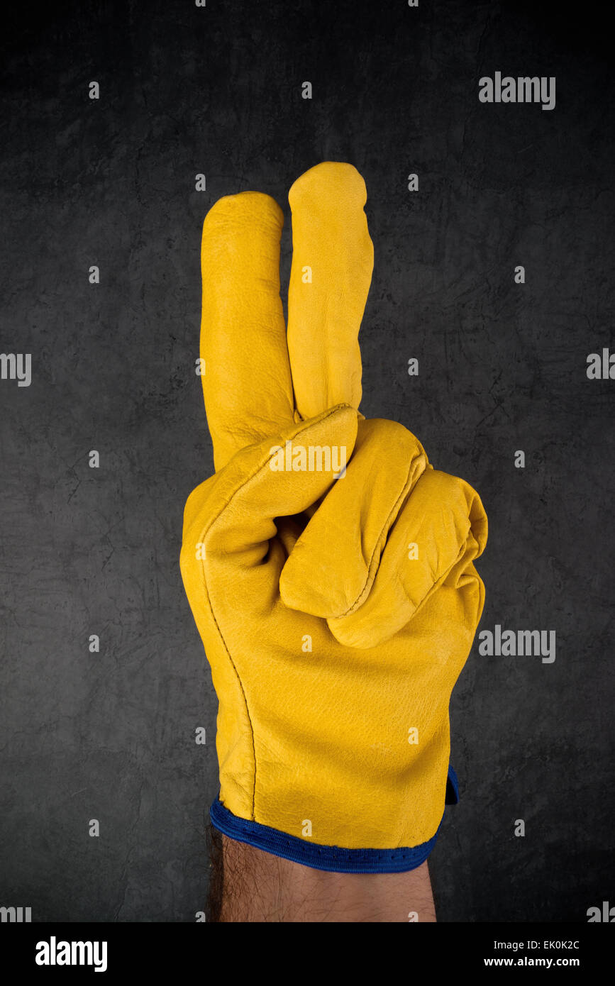 Männliche Hand in gelben Leder Bauingenieur oder Builder arbeiten schützende Handschuhe machen zwei Finger Geste. Stockfoto