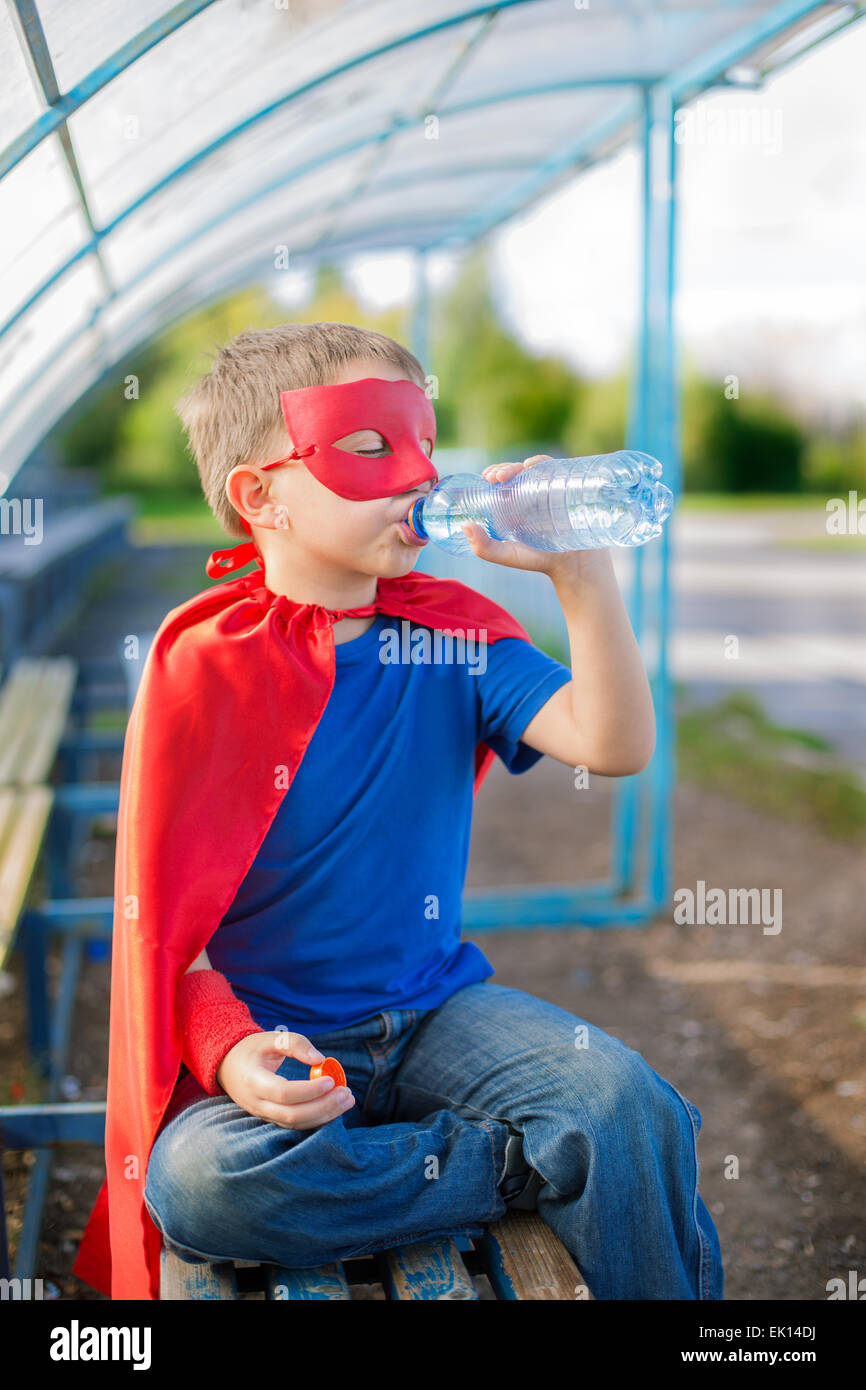 Junge gekleidet in Cape und Maske Trinkwasser aus der Flasche Stockfoto