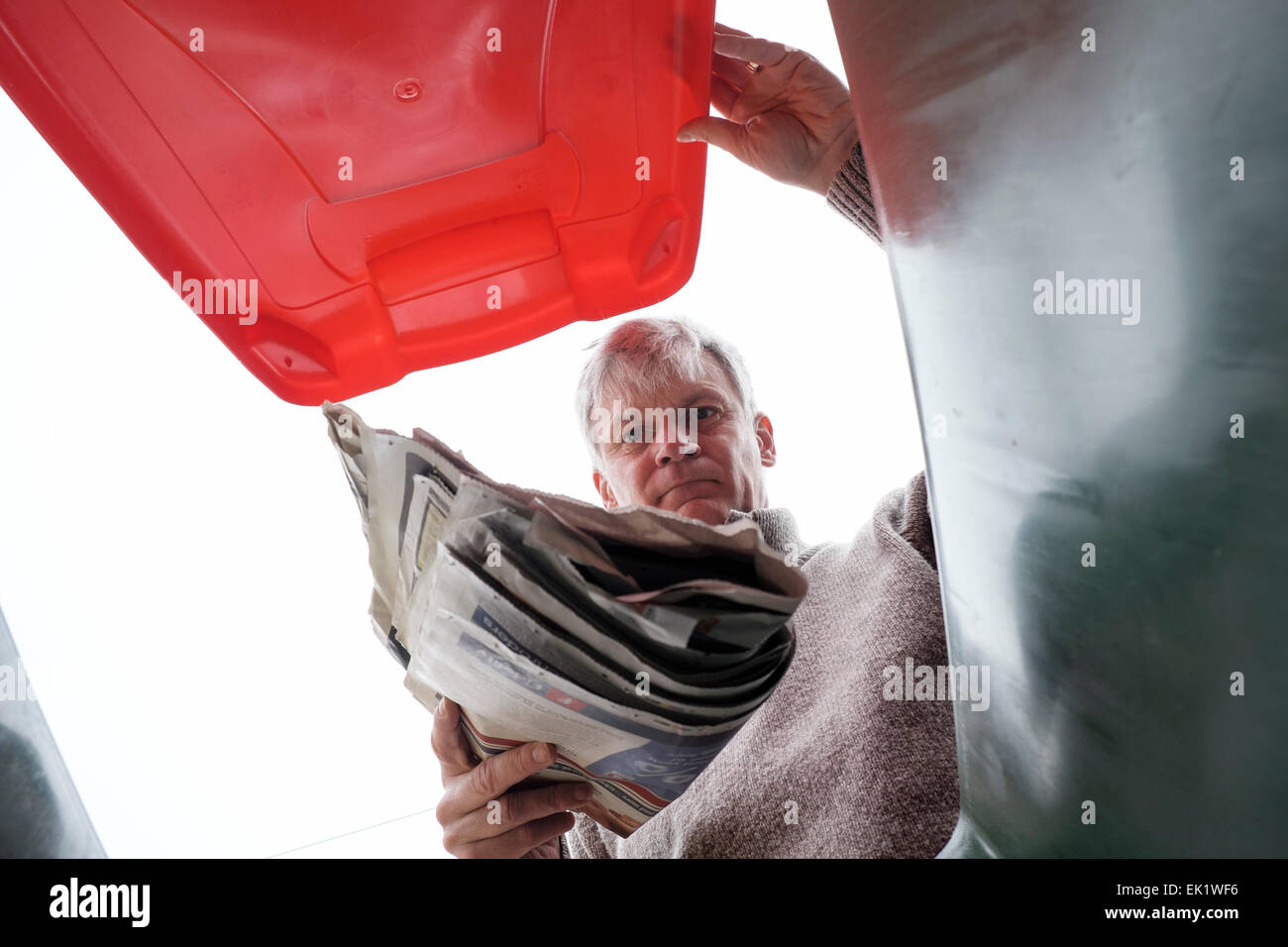 Mann, die Zeitung in den Hausmüll recycling Behälter fallen Stockfoto