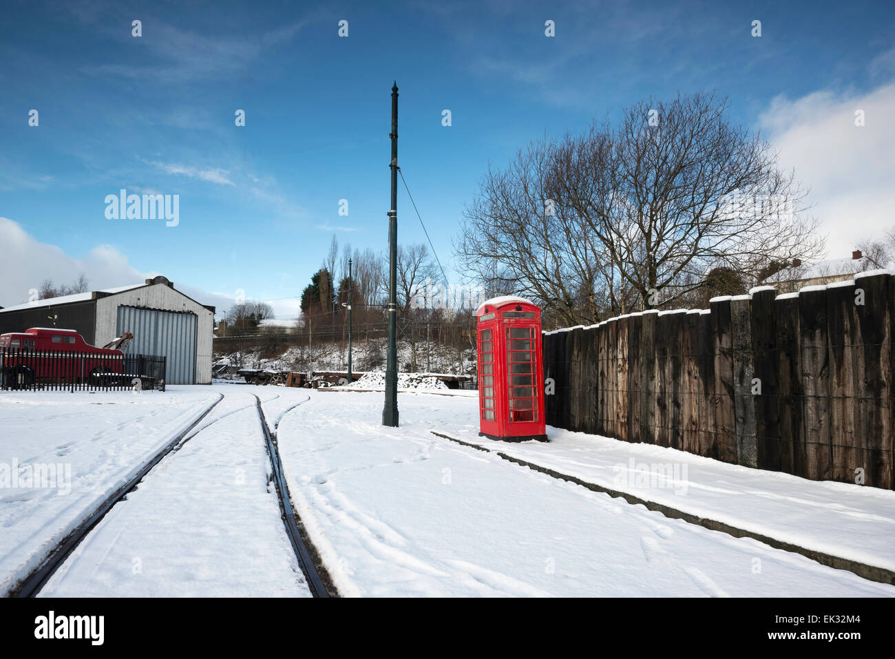 Rote Telefonzelle auf tief verschneiten Straße in Summerlee Industrial Heritage Museum. Eisenbahn-Straßenbahn-Linien durch den Schnee. . Stockfoto