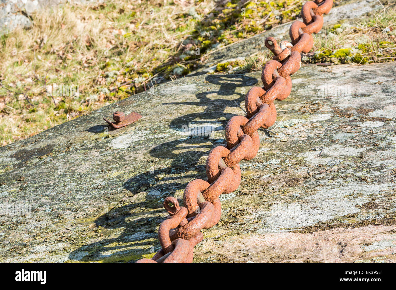 Alten, großen rostigen Eisenkette auf Granit Hügel. Sonnenlicht erzeugt feine Schatten auf Felswand. Links sind doppelt. Stockfoto