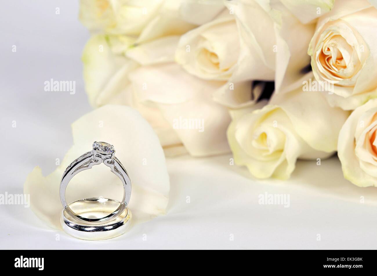 Diamant-Verlobungsring und Ehering auf weißen Rosenblüte mit Bouquet. Stockfoto
