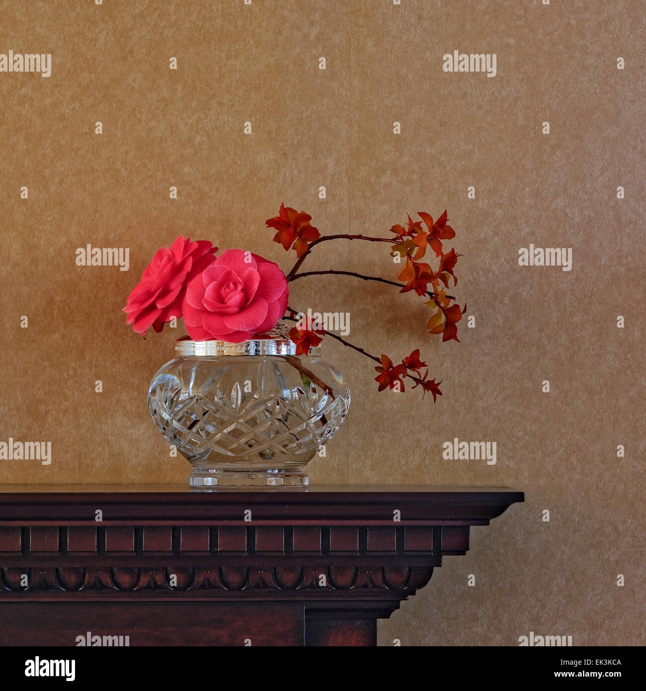 Blumenarrangements, einschließlich kamelie Blumen in einer Vase auf ​Crystal aus Holz geschnitzte Kaminsims gegen normale Tapete, quadratischen Format. Stockfoto