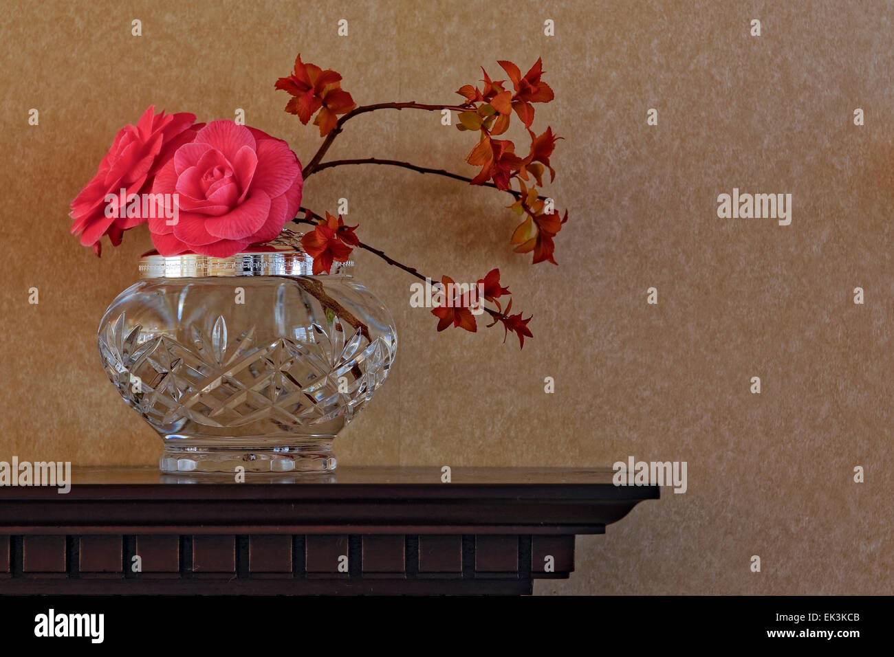 Blumenarrangements, einschließlich kamelie Blumen in einer Vase auf Crystal aus Holz geschnitzte Kaminsims gegen normale Tapete, Querformat. Stockfoto