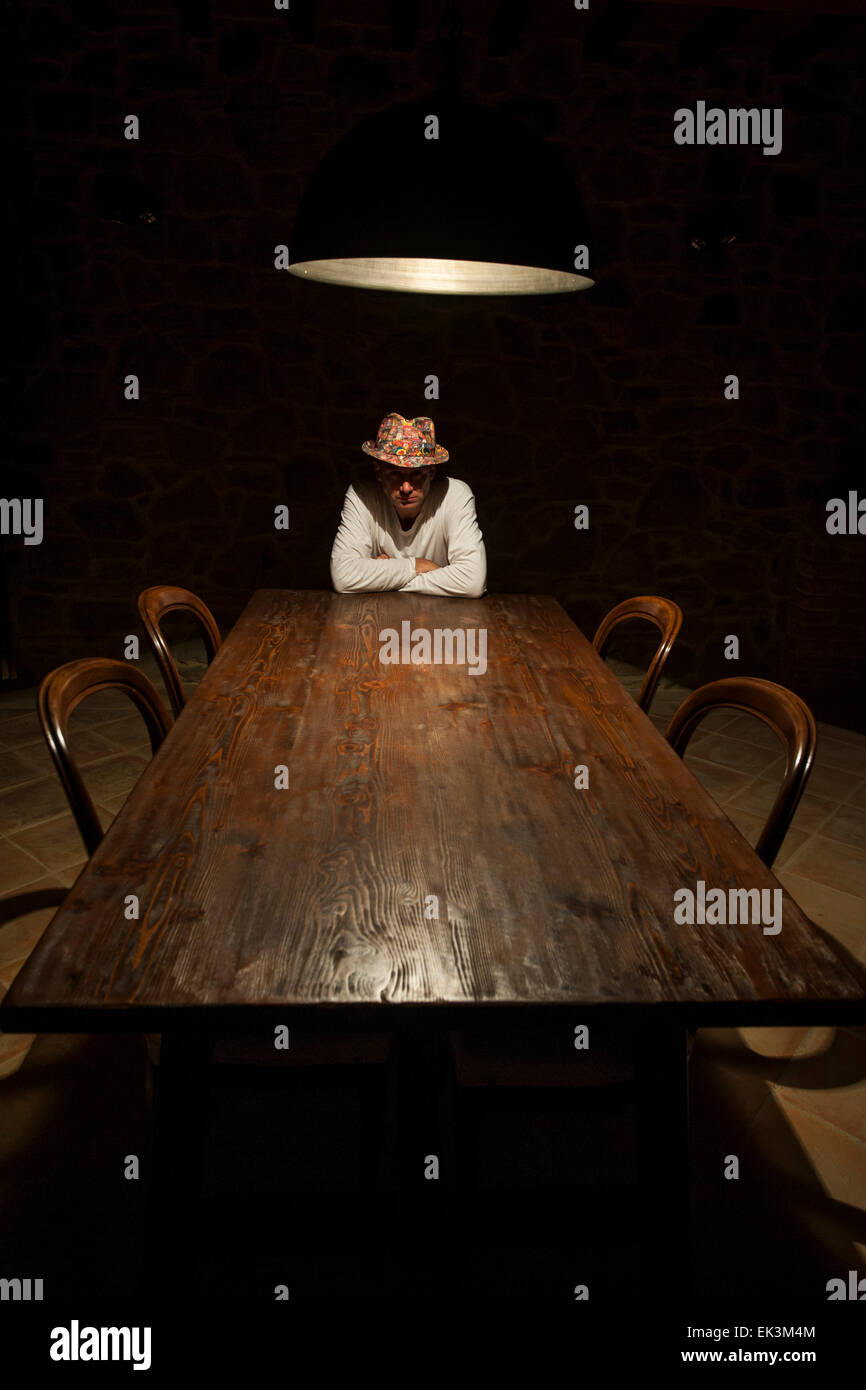Ein Mann sitzt unter einem starken Licht an einem langen Tisch Stockfoto