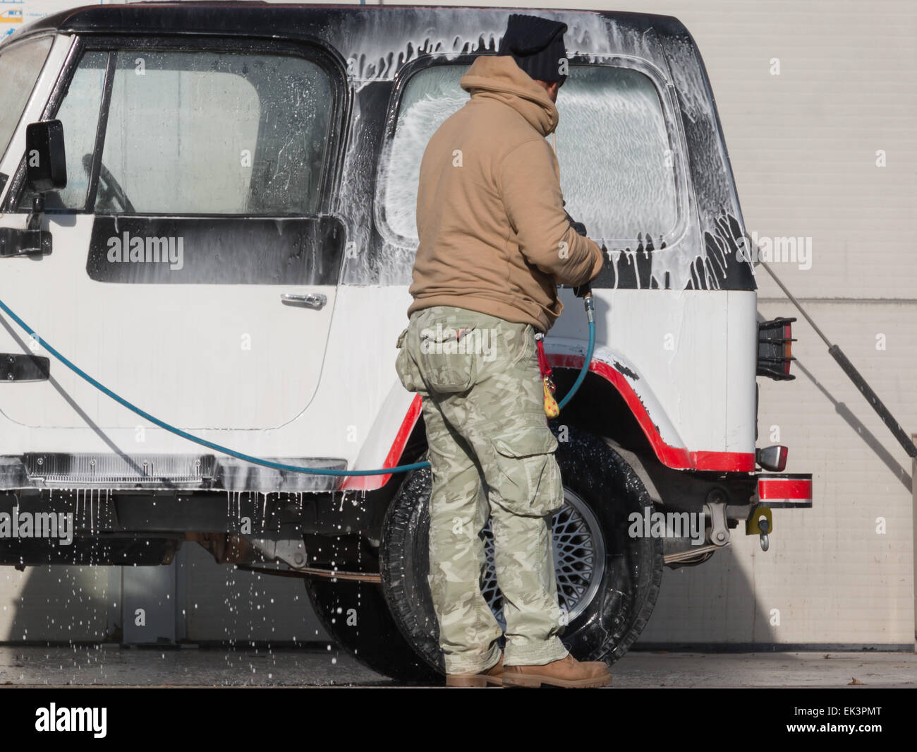 Mann sein Auto mit einem Strahl aus Wasser und Shampoo zu waschen Stockfoto