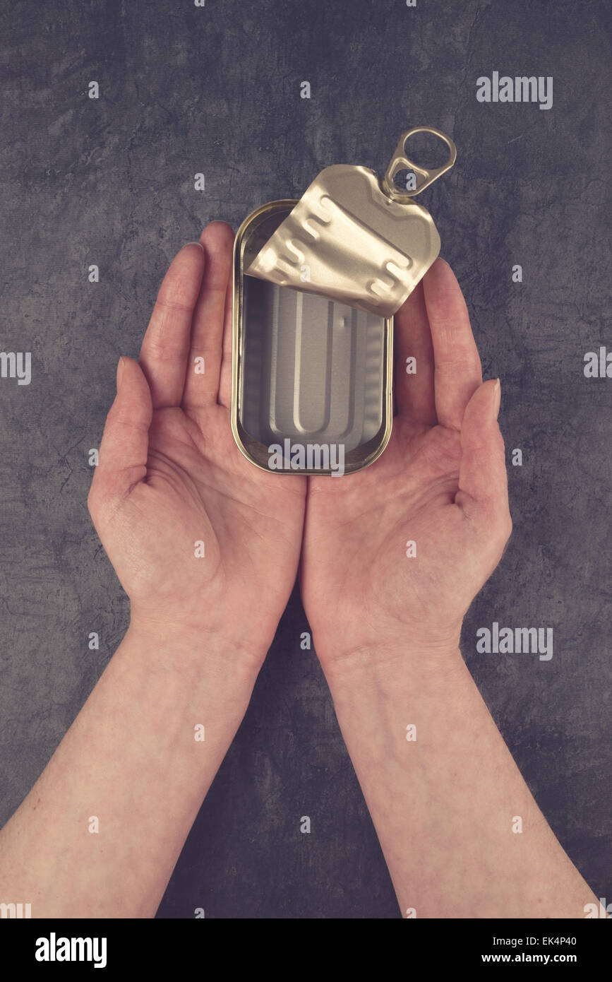 Weibliche Hände halten offene leere Sardine Fisch Blechdose auf Grunge grauer Hintergrund wie Armut und Hunger Konzept, Ansicht von oben Stockfoto