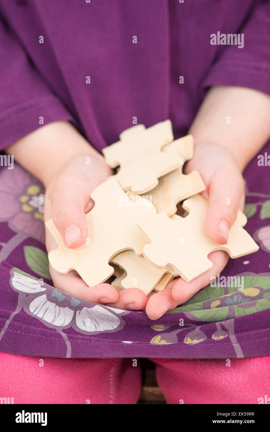 Kleines Mädchen (5 Jahre) Stücke von Holzpuzzle in ihren Händen hält. Konzeptbild von Kindheit Herausforderung, Zusammenarbeit und Stockfoto