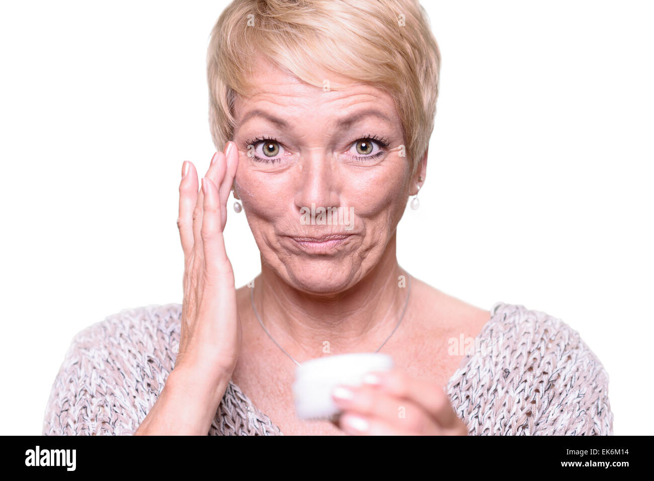 Im mittleren Alter attraktive blonde Frau, die die Falten um die Augen in dem Bemühen zur Bekämpfung der Hautalterung Anti-Aging-Creme zuweisen Stockfoto