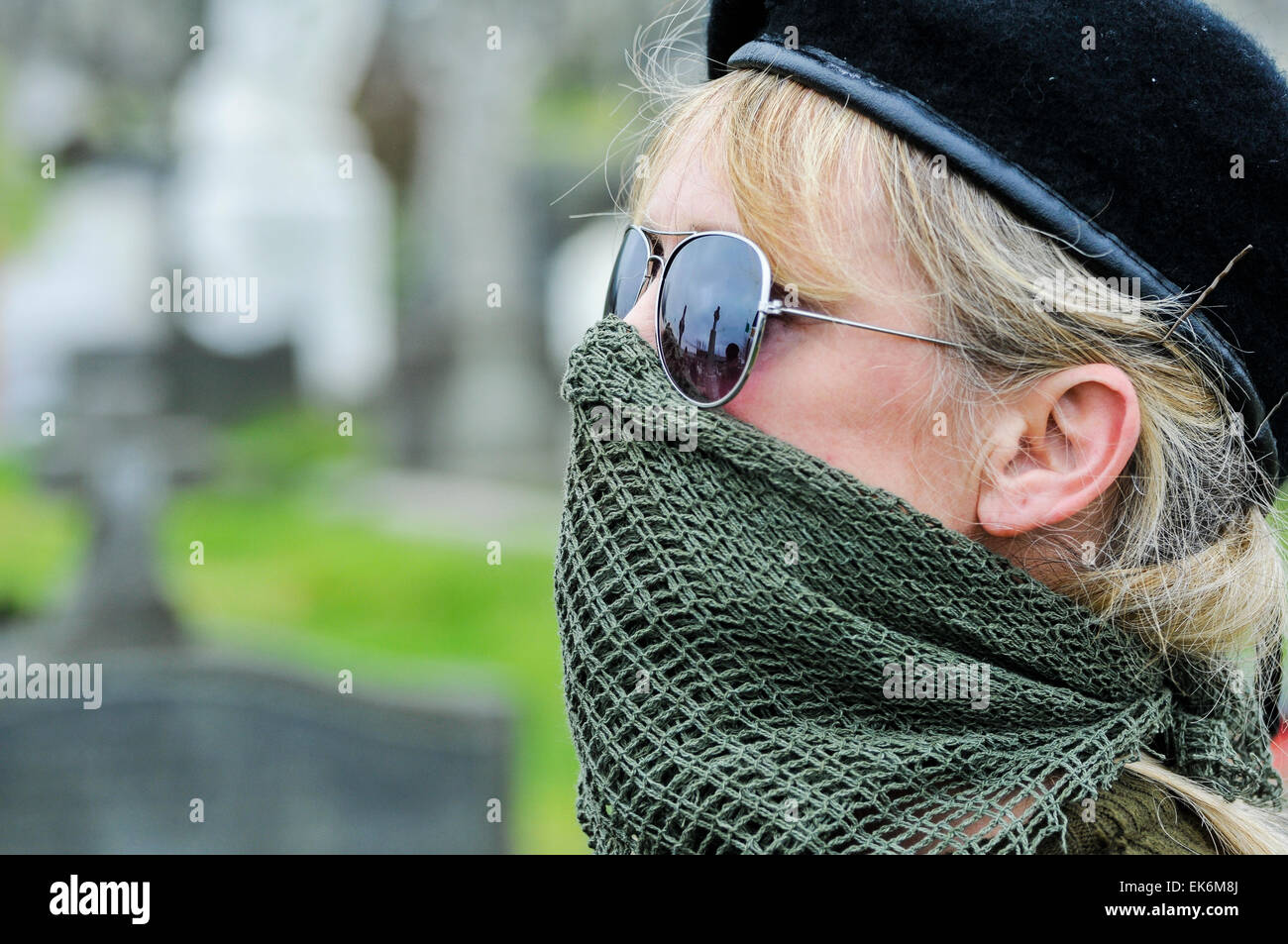 Eine maskierte Frau trägt ein Gelege vor den Mund, Sonnenbrille und eine schwarze Baskenmütze gehört ein Irish Republican Gedenken Stockfoto
