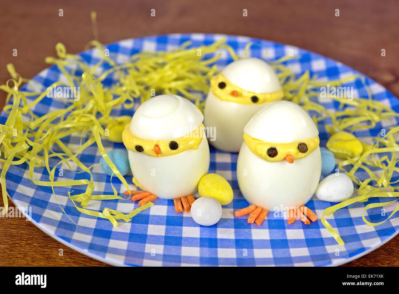 Ostern deviled Egg Küken mit Süßigkeiten Eiern und gelben Grases auf blau-weiß karierten Teller. Stockfoto