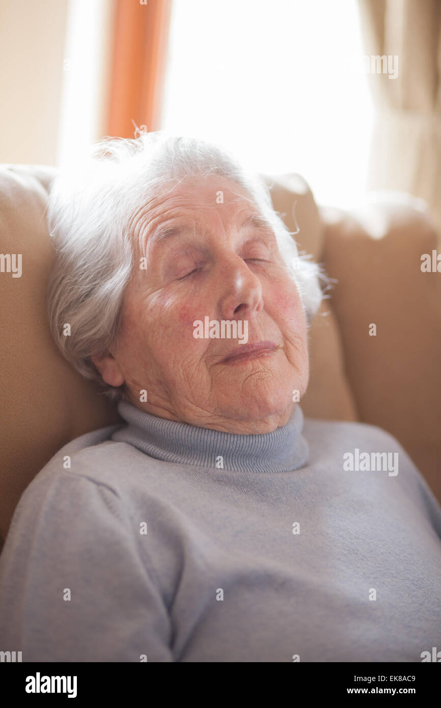 Alte Dame schlief aufrecht im Sessel mit zufriedenen Lächeln Stockfoto