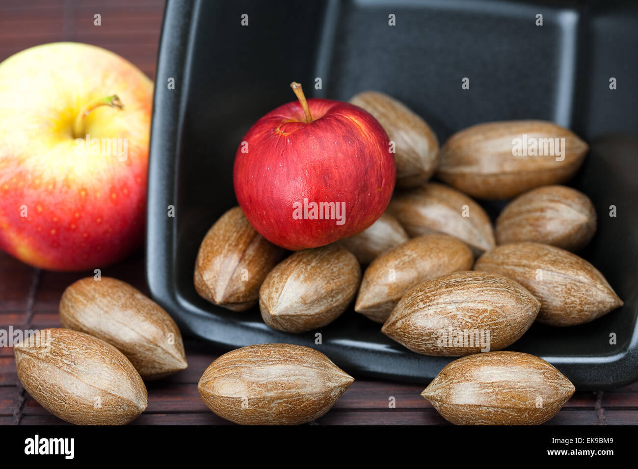Pekannüsse und Äpfel in einer Schüssel auf einer Bambusmatte Stockfoto