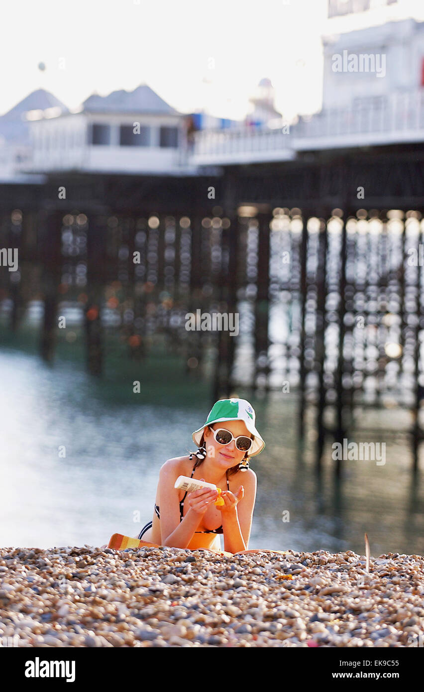 Junge Frau, die Anwendung von Sonnencreme mit Bikini am Strand Brighton UK Stockfoto