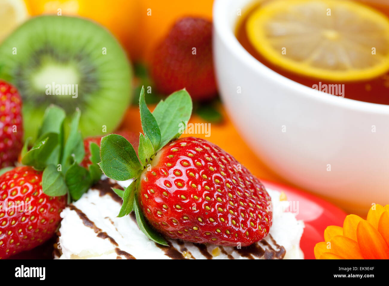 Tee mit Zitrone, Mandarine, Kiwi, Kuchen und Erdbeeren liegen auf der ora Stockfoto
