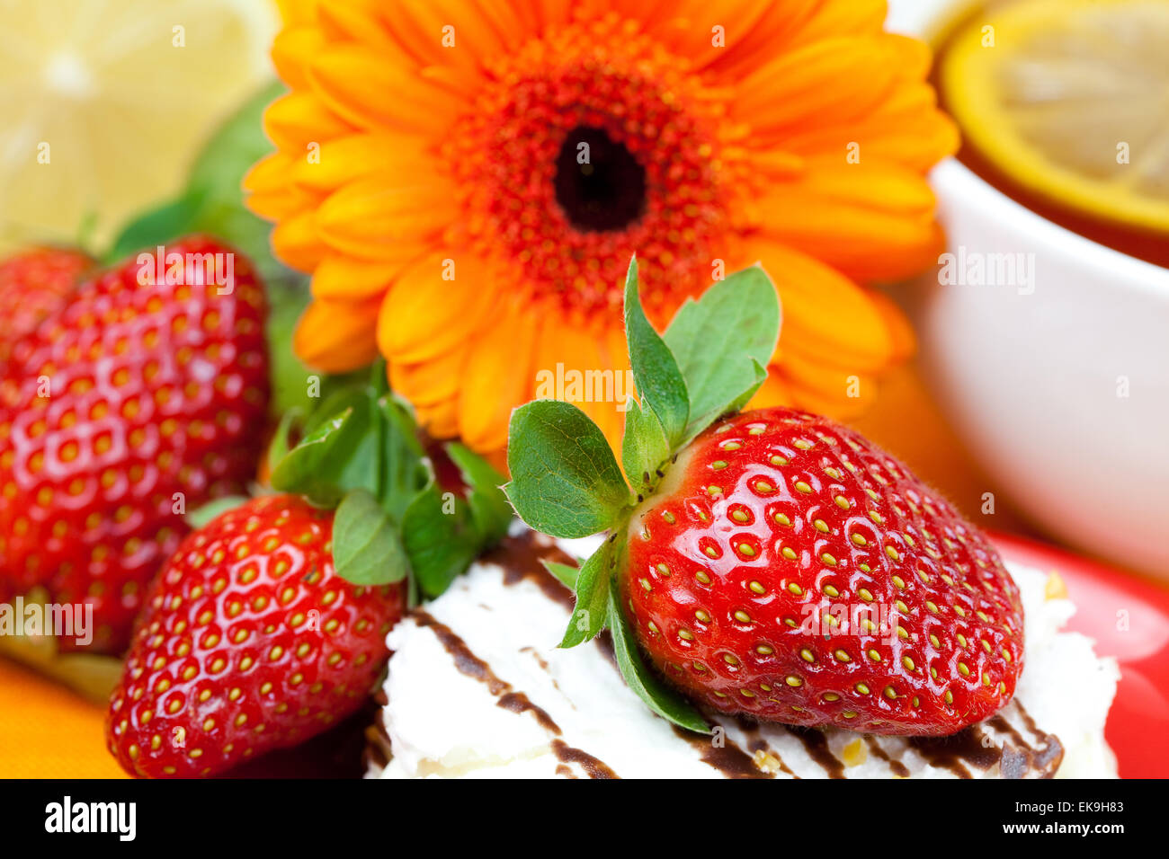 Tee mit Zitrone, Gerbera, Kuchen und Erdbeeren liegen auf der orange i Stockfoto