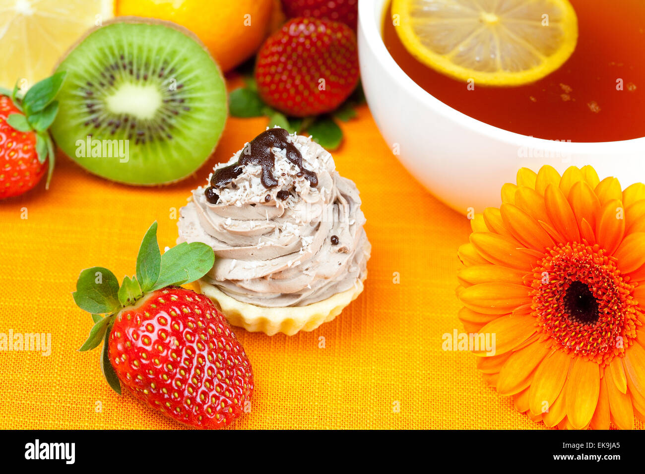 Gerbera, Tee mit Zitrone, Mandarine, Kiwi, Kuchen und Erdbeeren auf t liegend Stockfoto