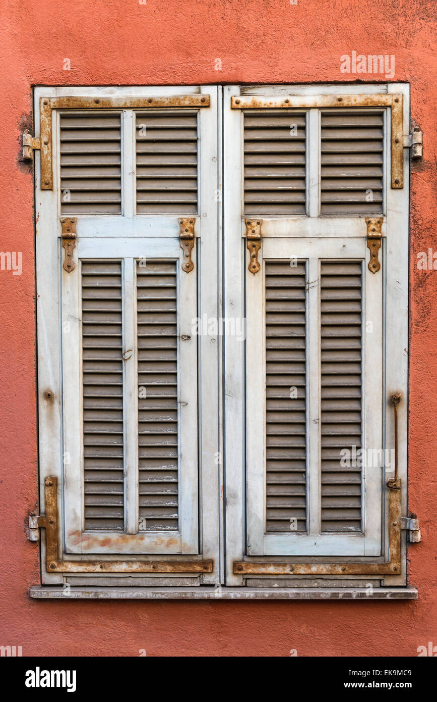 Weiße verwitterte französischen hölzernen Fensterläden auf einer roten Wand Stockfoto
