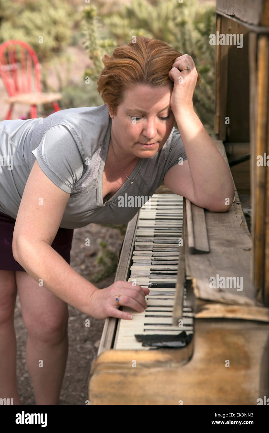Reife Frau inmitten der Wüste eine hölzerne, antike Klavierspiel mit einem traurigen, kontemplativen Ausdruck Stockfoto