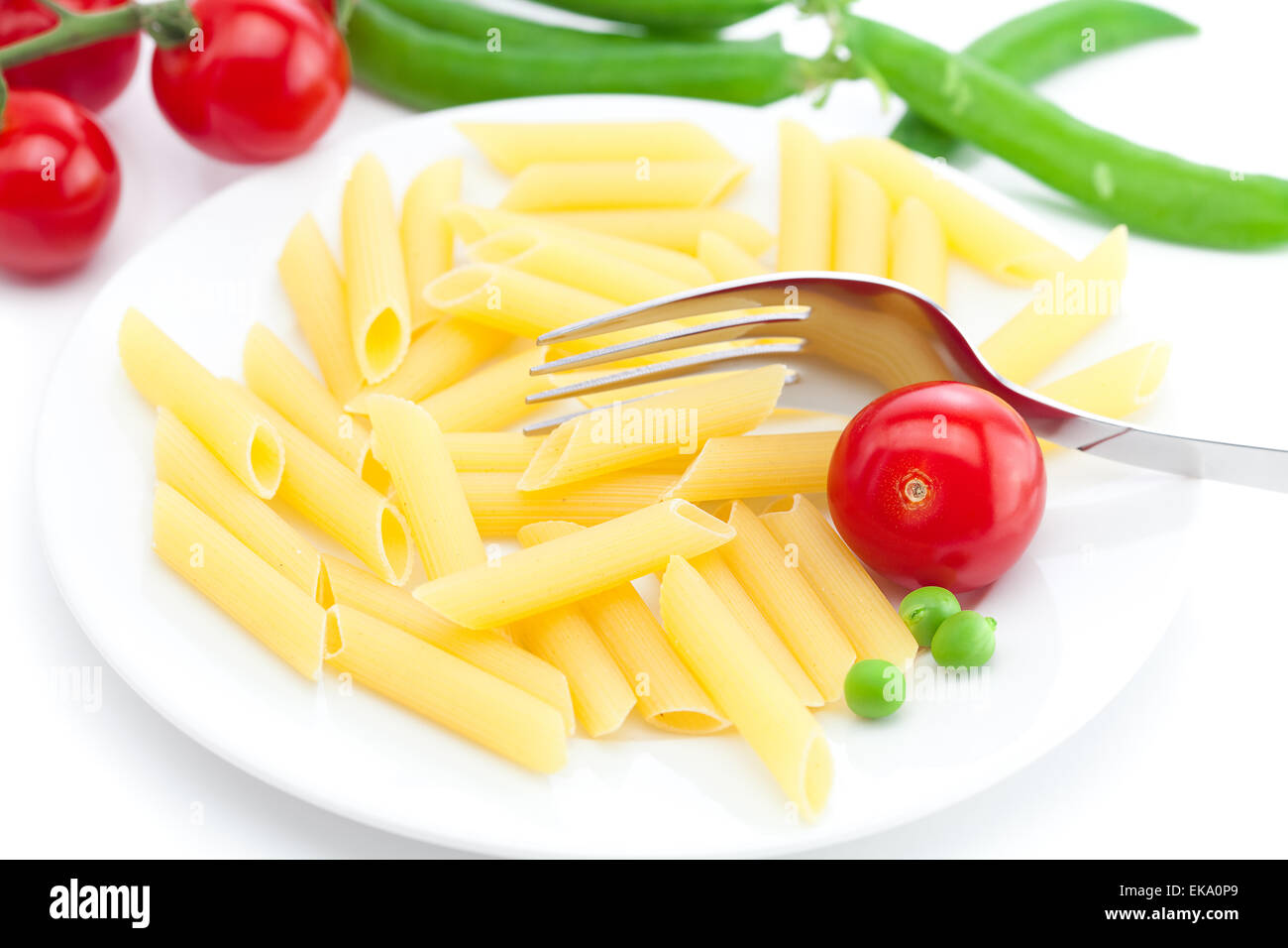 Tomaten, Erbsen, Nudeln und Gabel auf einem Teller isoliert auf weiss Stockfoto