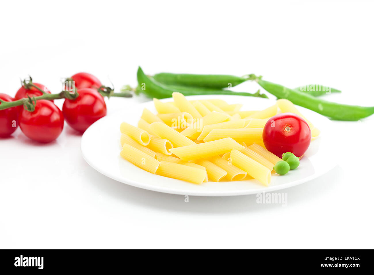 Tomaten, Erbsen und Nudeln auf einem Teller isoliert auf weiss Stockfoto