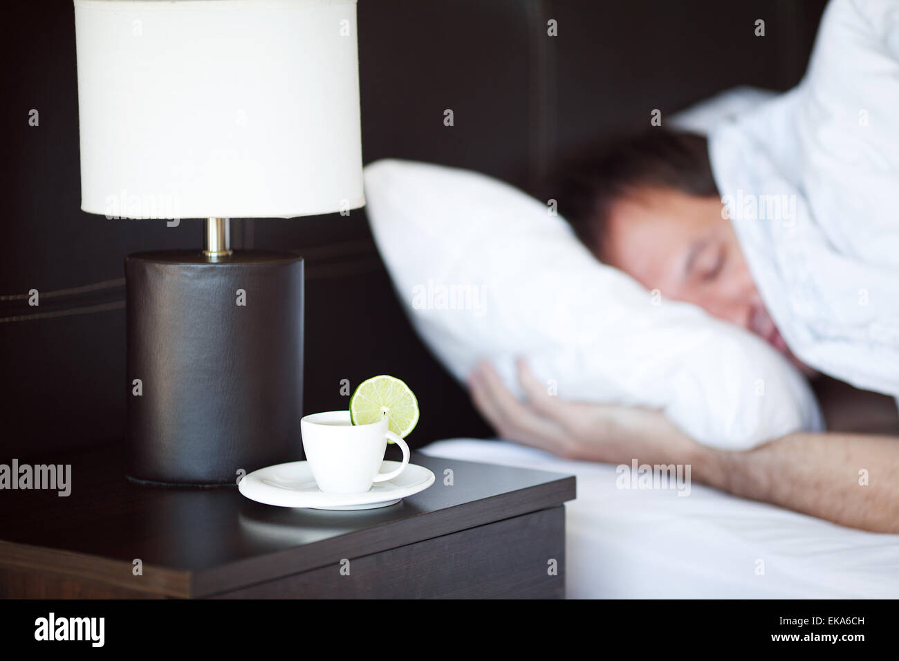 Mann schläft auf einem Bett, einer Tasse Tee auf dem Nachttisch und lam Stockfoto