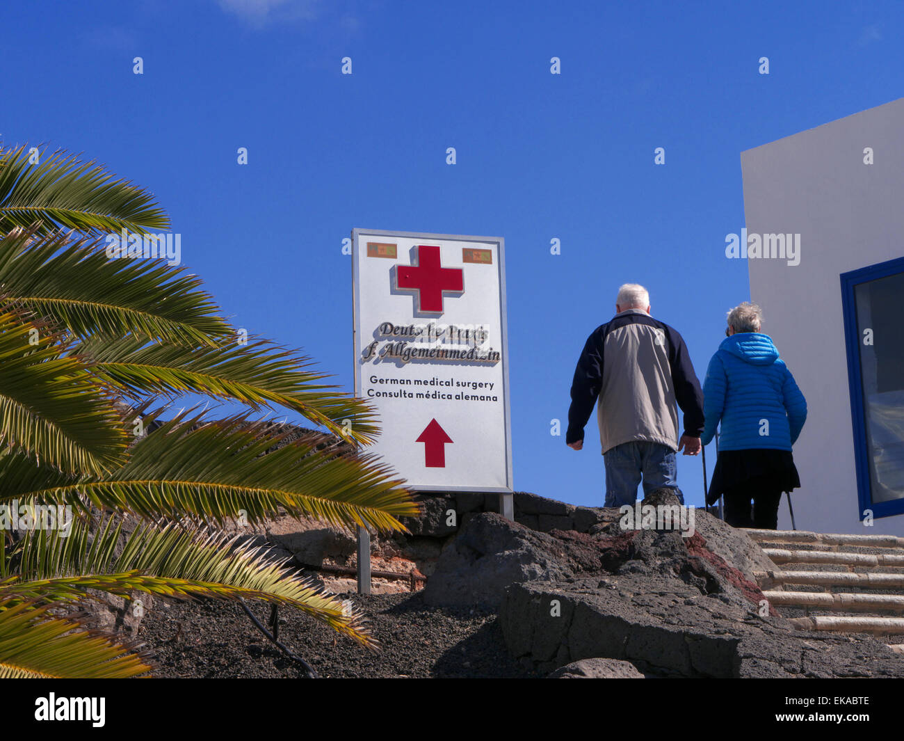 Medizinische Behandlung für die Krankheit im Ausland älteres Ehepaar und Zeichen für die lokale private Klinik Pflege in Kanaren Spanien EU mit blauem Himmel & Palmen Stockfoto