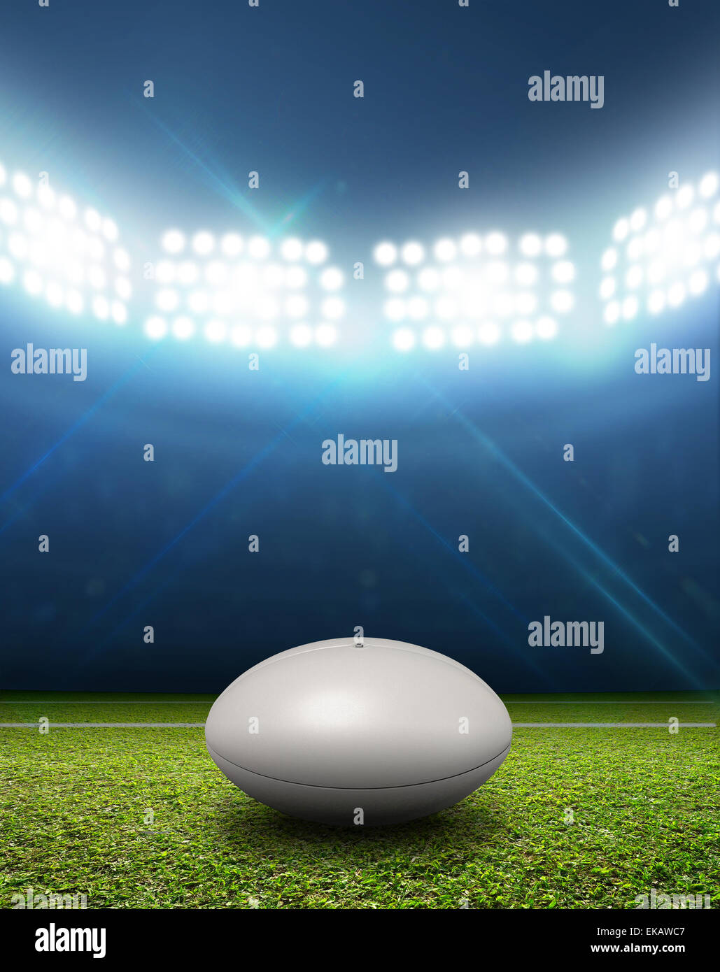 Ein Rugby-Stadion mit einem generischen weißen Rugby-Ball auf einem markierten grünen Rasenplatz in der Nacht unter Flutlicht beleuchtete Stockfoto