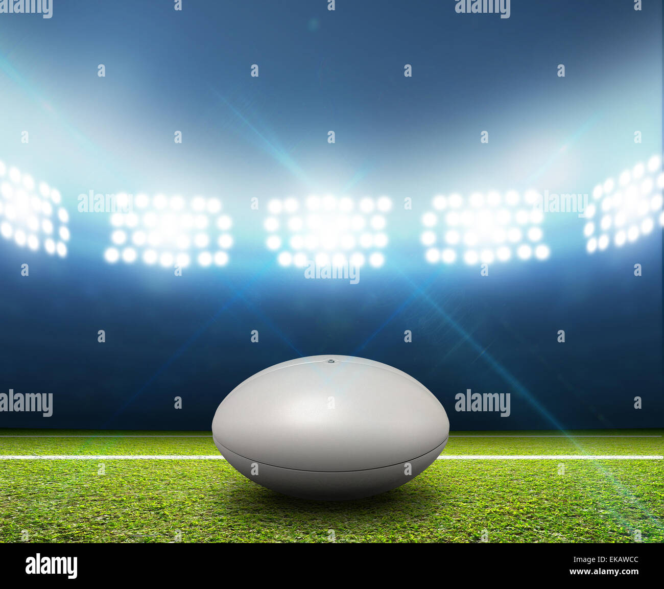 Ein Rugby-Stadion mit einem generischen weißen Rugby-Ball auf einem markierten grünen Rasenplatz in der Nacht unter Flutlicht beleuchtete Stockfoto