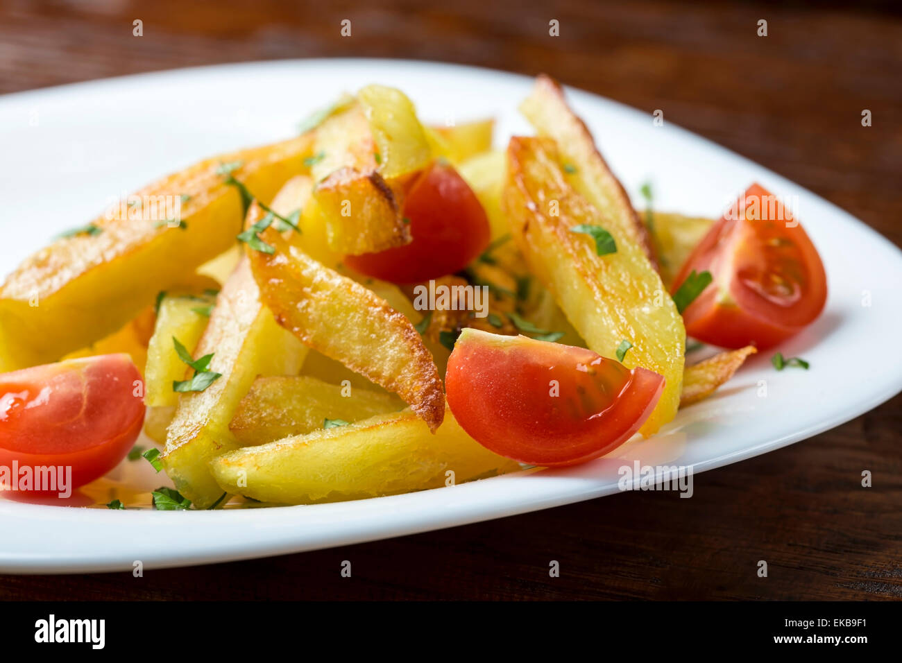 Bratkartoffeln mit Cherry-Tomaten in weiße Schale über Holztisch Stockfoto