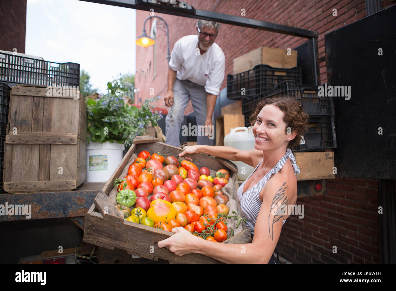 Landwirte, die Kisten mit Bio-Tomaten außerhalb Lebensmittelgeschäft entladen Stockfoto