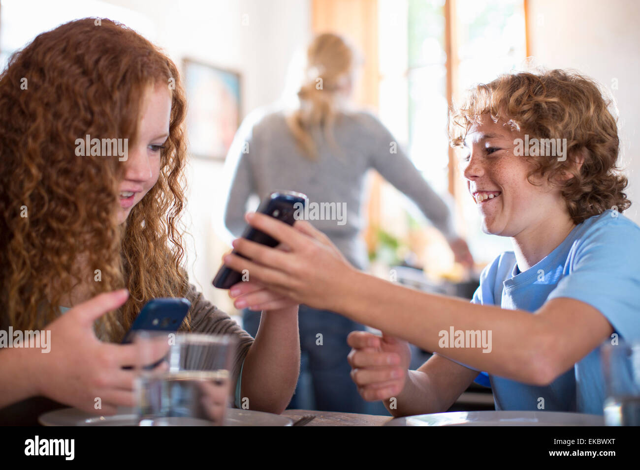 Geschwister mit Smartphone am Esstisch Stockfoto