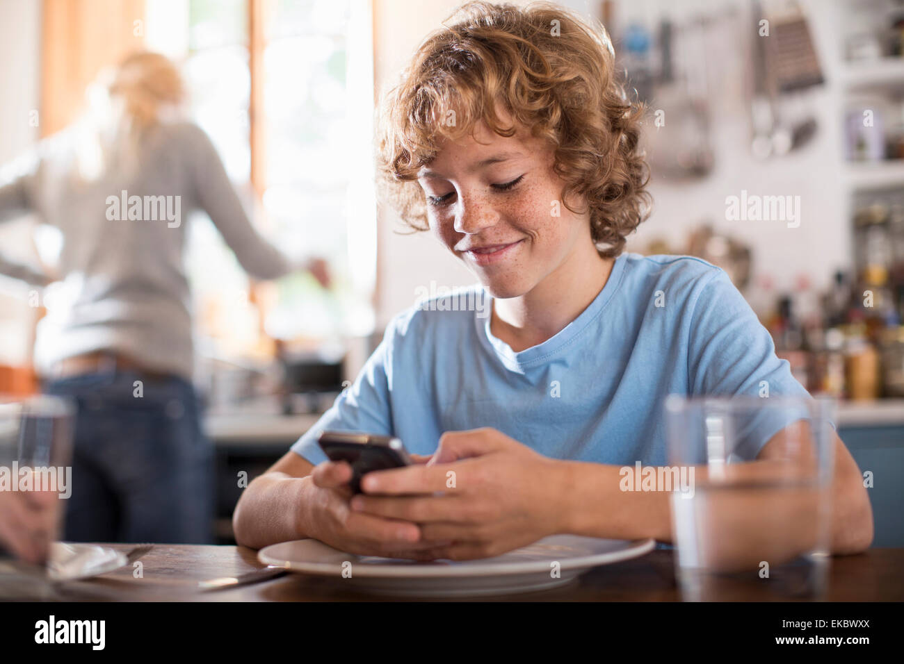 Teenager mit Smartphone am Esstisch Stockfoto