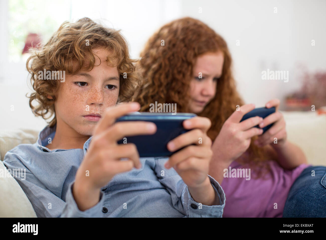 Geschwister spielen mit Handheld-Computer-Spiel auf couch Stockfoto