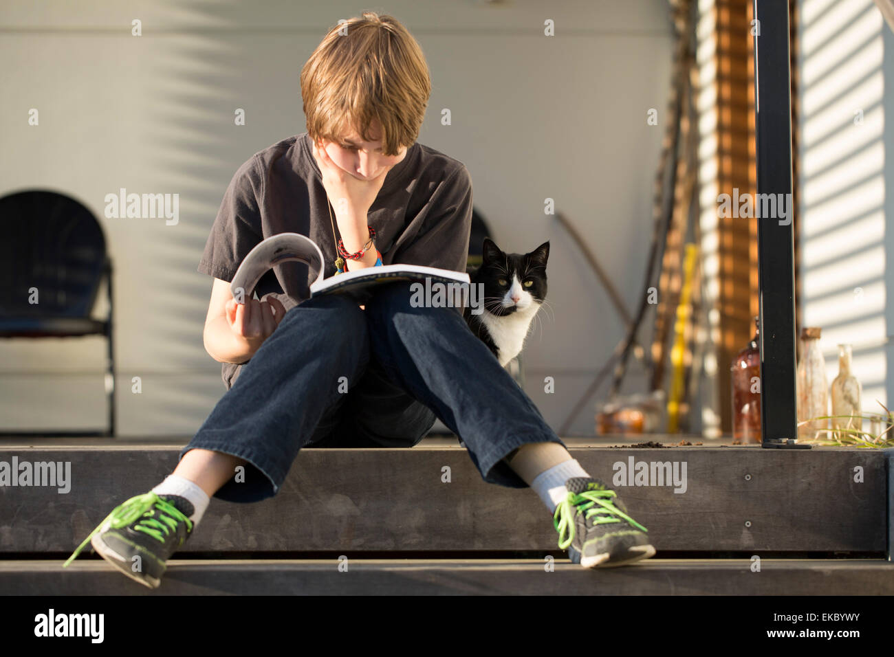 Junge sitzt auf Schritt Lesebuch, Katze peering von hinten Stockfoto
