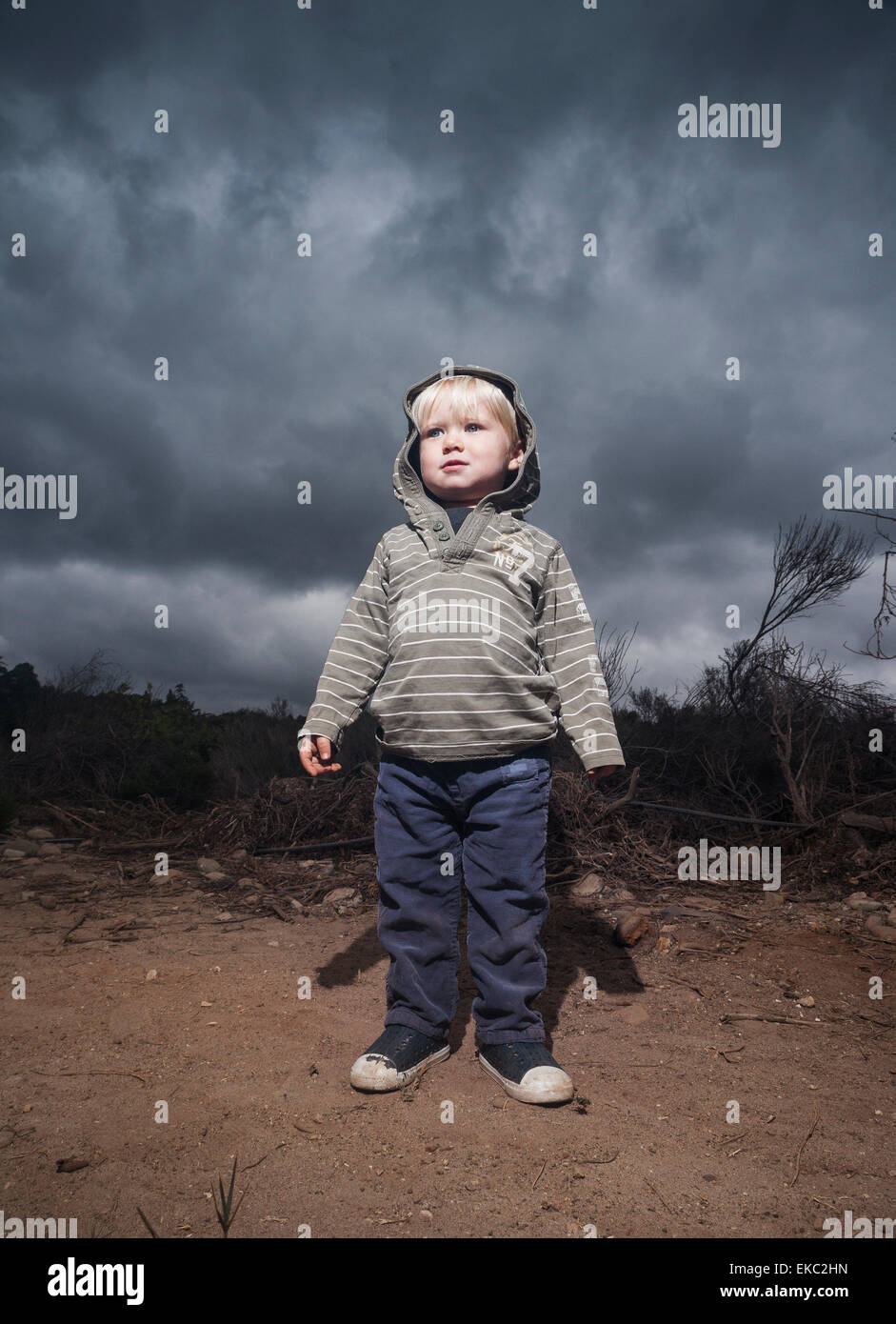 Kleiner Junge stehend gegen stürmischen Himmel Stockfoto