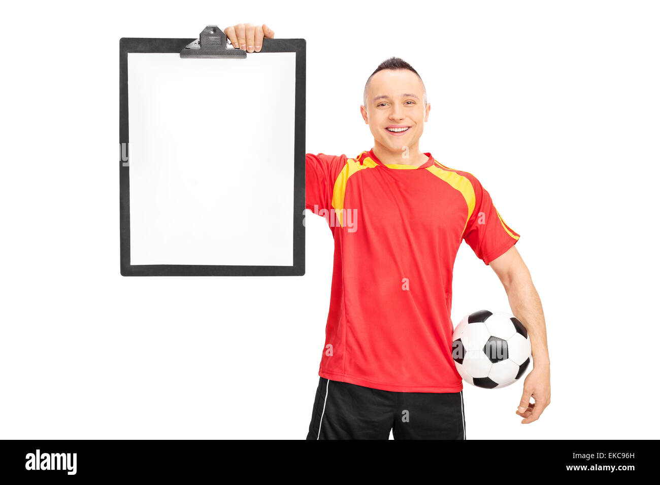 Junger Fußballspieler in einem roten und gelben Trikot mit einem Klemmbrett und einer Kugel isoliert auf weißem Hintergrund Stockfoto