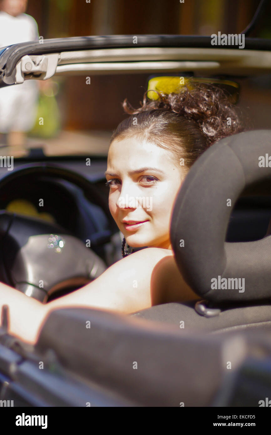 Lächelnde junge Frau auf der Suche über die Schulter in ein Cabrio Stockfoto