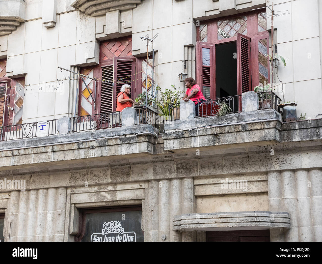 Zwei weibliche Erwachsene kubanischen Nachbarn, beide tragen roter Pullover, während auf den Balkonen ihrer zweiten Geschichte Wohnungen sprechen. Stockfoto