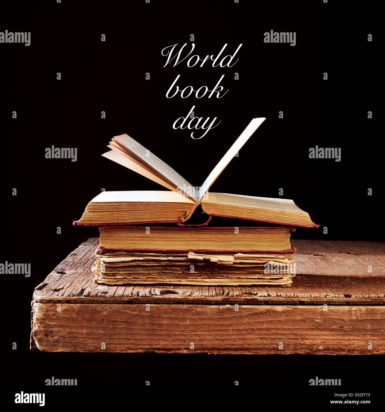einige alte Bücher auf einem rustikalen Holztisch und den Text Welttag des Buches geschrieben in weiß auf schwarzem Hintergrund Stockfoto