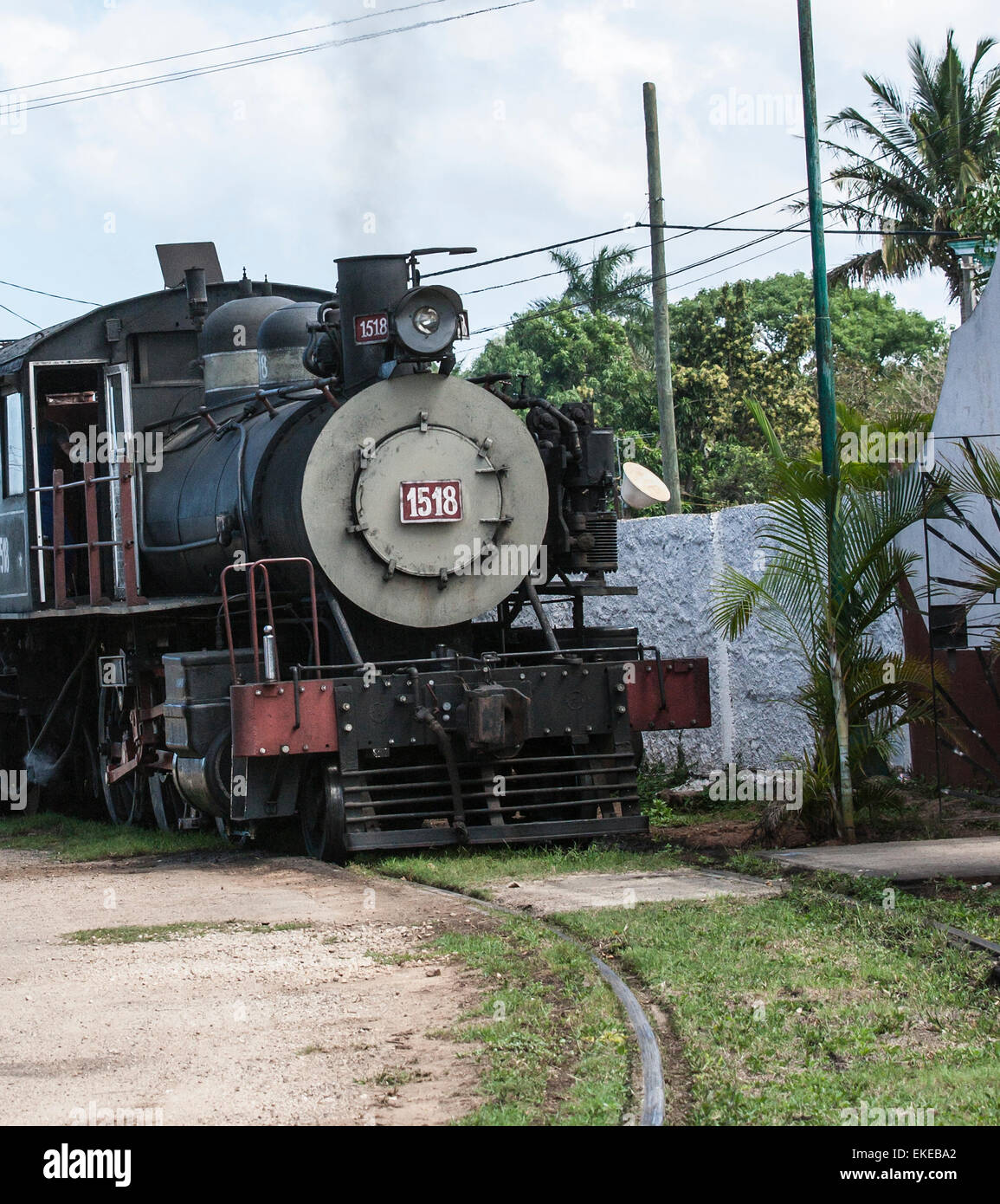 Alte restaurierte amerikanische Dampfzug in Kuba mit Dampf und Palmen und der Bahnstrecke im Vordergrund Stockfoto