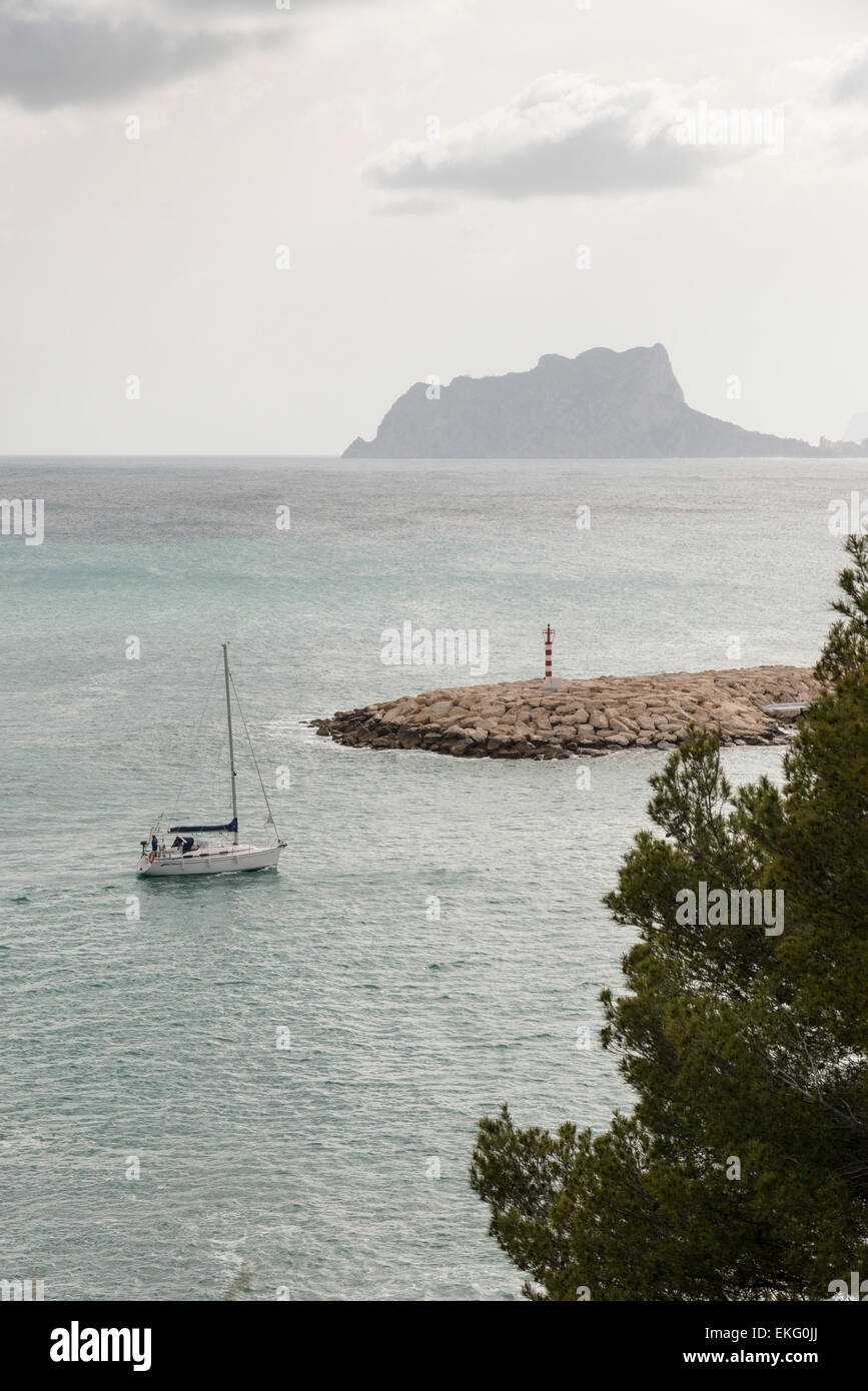 Eine Segelyacht tritt in den Hafen von Moriara an der Costa Blanca in Spanien mit Ifach Felsen im Hintergrund Stockfoto