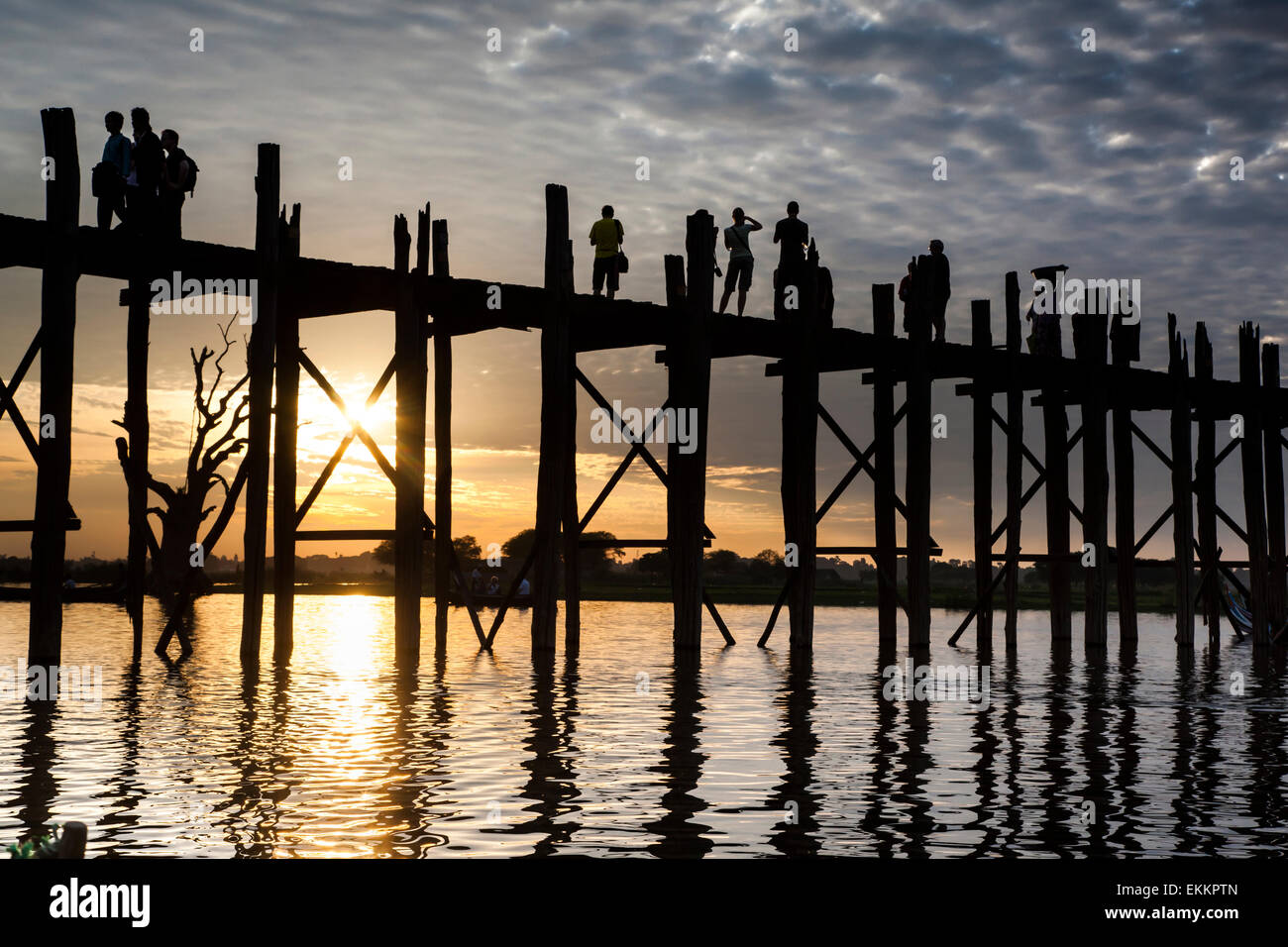 Silhouette Persönlichkeiten, darunter eine Frau in kurzen Hosen, fotografieren, auf die U Bein Brücke über Taungthaman See bei Sonnenuntergang. Stockfoto