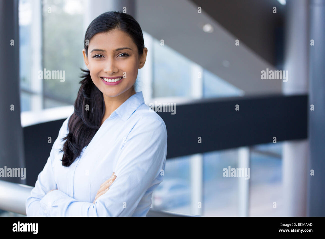Closeup Portrait, gefaltet junge professionelle, schöne selbstbewusste Frau im blauen Hemd, verschränkten Armen, lächelnd isoliert im Haus aus Stockfoto