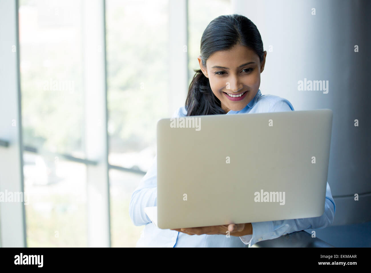 Closeup Portrait, junge, attraktive Frau, Mutter, stehen, lächelnd auf der Suche, den silbernen Laptop surfen. Isolierte Glasfenster in Stockfoto