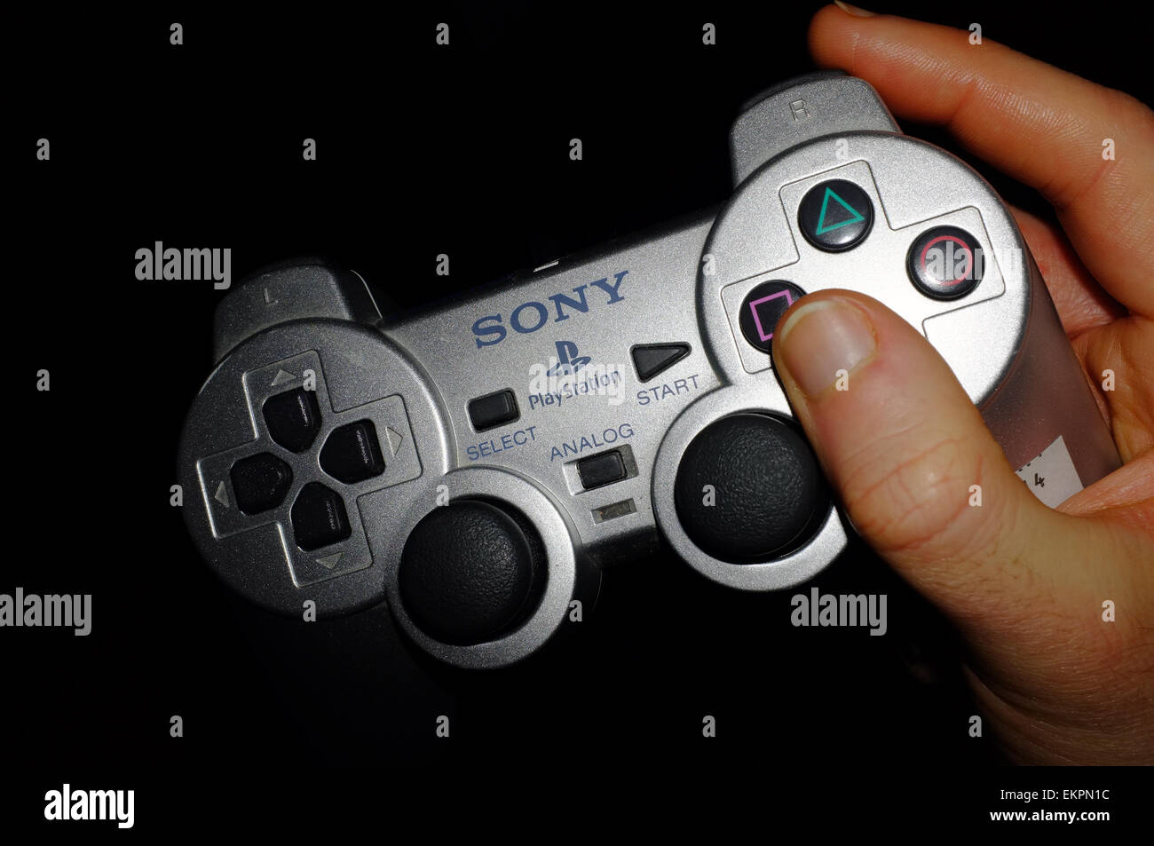 Eine weiße Hand, die einen Playstation-Controller vor schwarzem Hintergrund Stockfoto