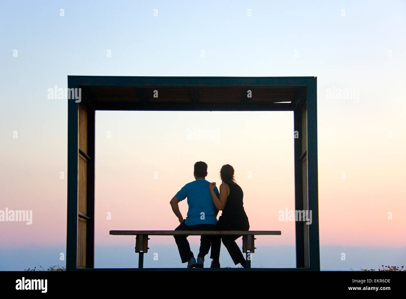 Touristen sitzen auf Bank mit einem Türrahmen am Strand, Paphos (Pafos) bei Sonnenuntergang, Republik Zypern Stockfoto