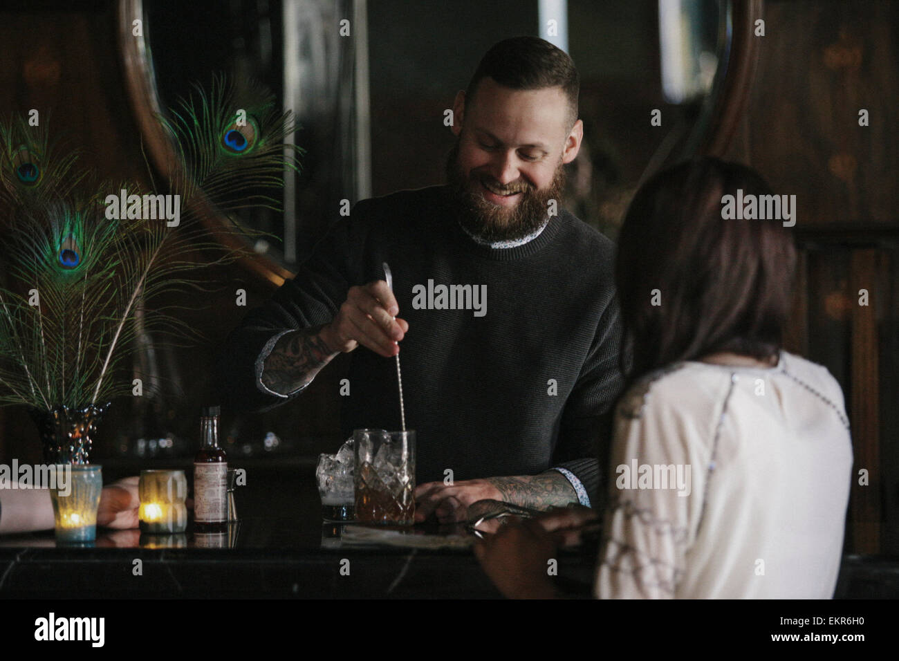 Eine Frau und ein Barkeeper sprechen, und Getränke mischen. Stockfoto