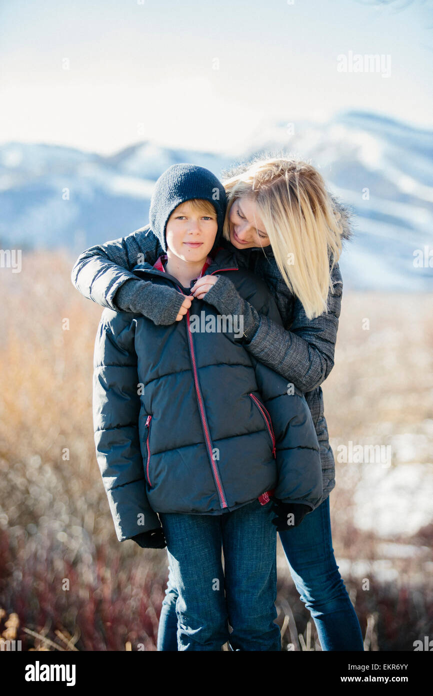 Ein Junge in einer Jacke und Woolly Hut wird von seiner Mutter umarmte. Stockfoto