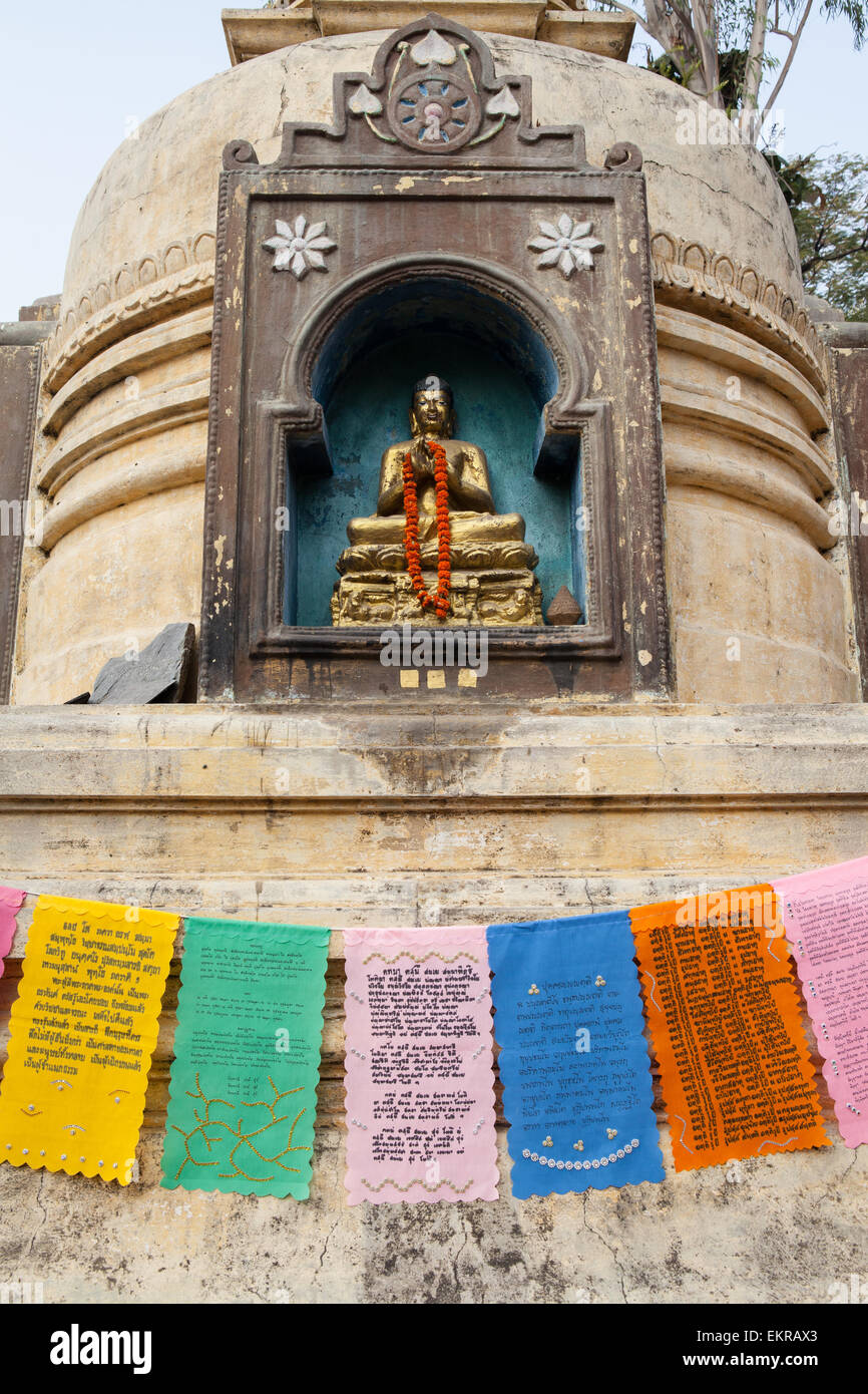 Ein Chorten und Stupa mit einer Statue des Buddha mit Gebetsfahnen im Mahabodhi Tempel Complex in Bodhgaya Stockfoto